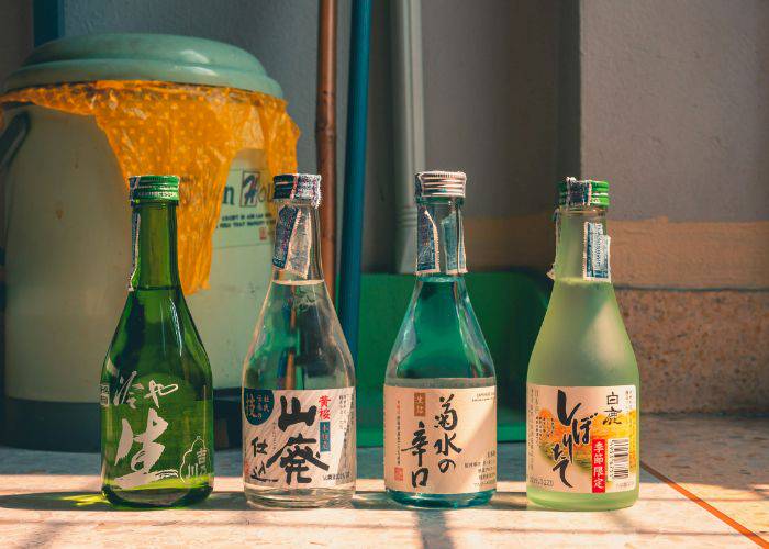 Four bottles of sake on a sunny counter or floor, lit gently by sunlight.